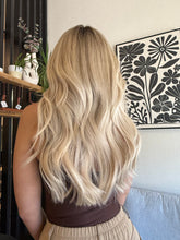 Load image into Gallery viewer, Person with long blonde hair sitting on a couch with a decorative pillow in the background.
